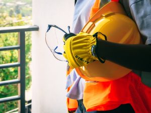 A construction worker holding safety equipment including eye protection, gloves, and a hard hat.